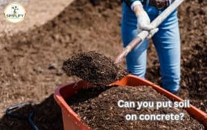 A man wearing gloves is carefully placing soil on a concrete surface with his hands, demonstrating the question, "Can you put soil on concrete?"